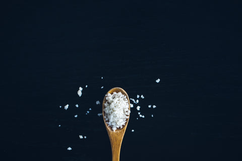 A wooden spoon filled with Medetarrenean sea salt crystal centred at the bottom of the image over a midnight blue background